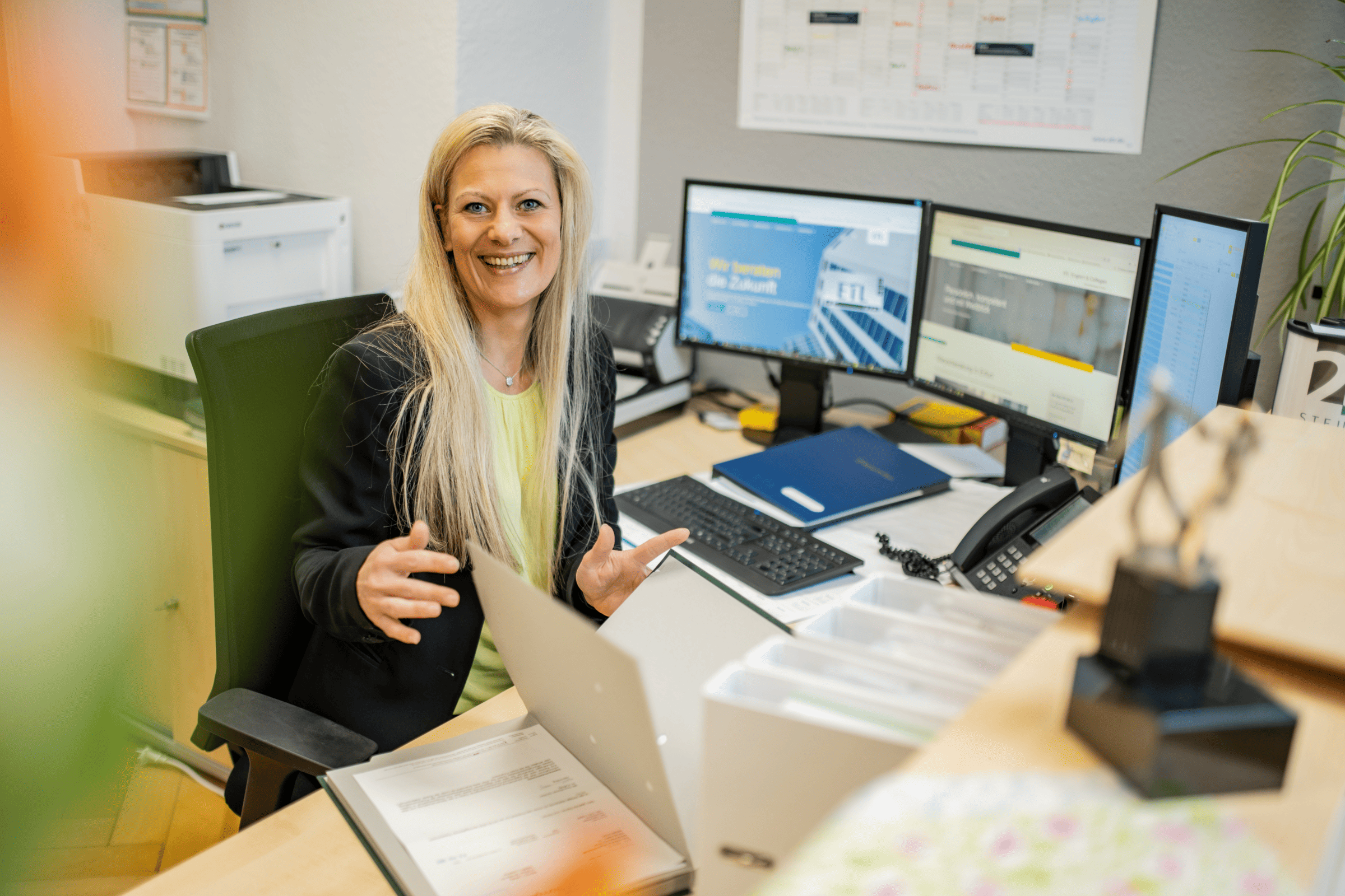 Frau am Arbeitsplatz mit 3 Bildschirmen bei ETL Englert & Collegen, die freundlich in die Kamera lacht